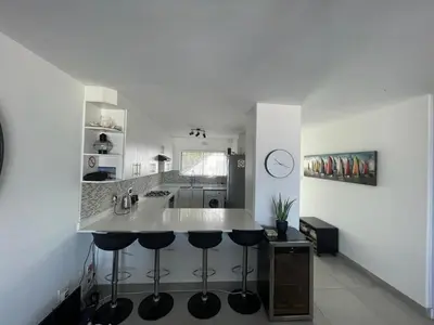 a kitchen with a white counter and stools in it at Blouberg Sea View in Bloubergstrand