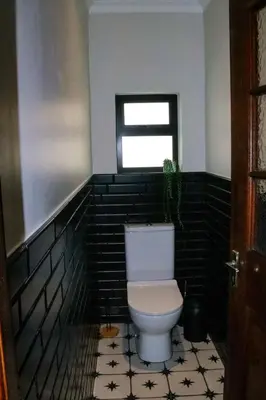a bathroom with a white toilet in a black tiled room at Villa Des Roses in Paarl