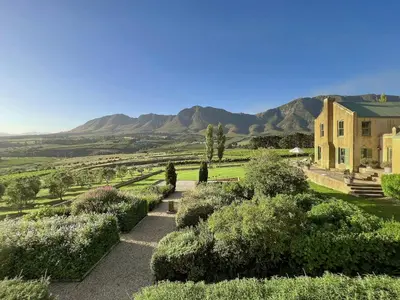 a house with a garden and mountains in the background at Moya's Vineyard in Mosselrivier