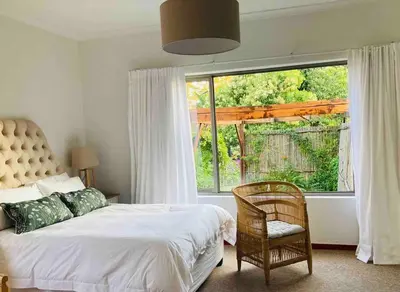 a bedroom with a bed and a chair and a large window at Garden studio close to Wine Farms in Somerset West