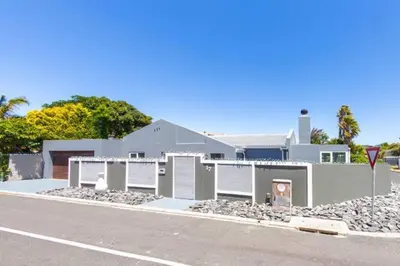 a white house with a pile of rocks next to a street at Family Home in West Beach, Blouberg in Cape Town