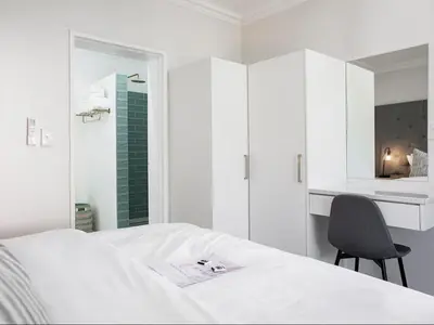 a white bedroom with a bed and a chair at La Dolce Vita Gordon’s Bay in Gordonʼs Bay