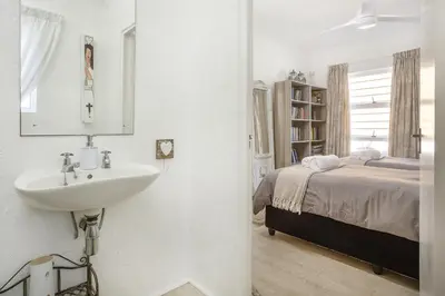 a white bathroom with a sink and a bed at Inn 201 in Hermanus