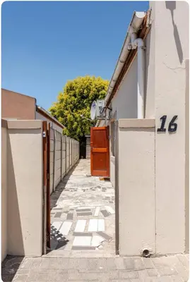 an alley with a white building with a brown door at A Room with private Entrance in Cape Town