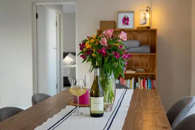 a bottle of wine and a vase of flowers on a table at Twin Gables, centrally located 2 bedroom apartment in Hermanus