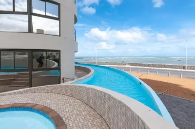 a building with a swimming pool next to the beach at Ocean View 304 Luxury Self Catering Apartment Strand Western Cape South Africa in Cape Town