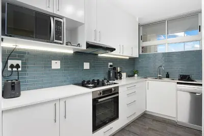 a kitchen with white cabinets and blue tiles at ZenDen Destinations' Tidal Tranquillity in Cape Town