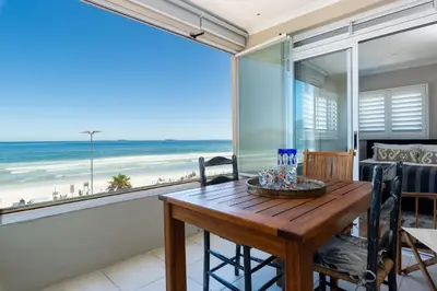 a dining room with a table and a view of the beach at Lagoon Beach Penthouse in Cape Town