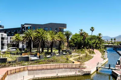 a park next to a river with palm trees and a building at Zals Luxury -Nine Palms in Cape Town