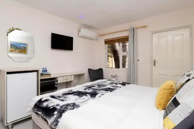 a white bedroom with a bed and a tv at Serena inn Room 1 in Cape Town