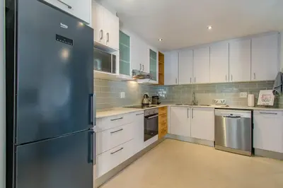 a large kitchen with white cabinets and a refrigerator at Chic, Cozy, Modern, Secure and Centrally Located in Cape Town