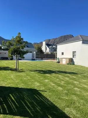a yard with a tree and a white house at Largest one bed apartment & private pool in the Hoek in Franschhoek