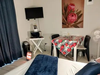 a room with a table and a bed and a television at Neptune in Gordonʼs Bay