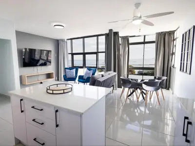 a kitchen and living room with white cabinets and blue chairs at St Tropez Beachfront 306 in Strand