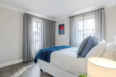 a bedroom with a white bed with blue sheets and windows at Songbird D'Aria Cape Town luxury house on Wine Estate in Cape Town