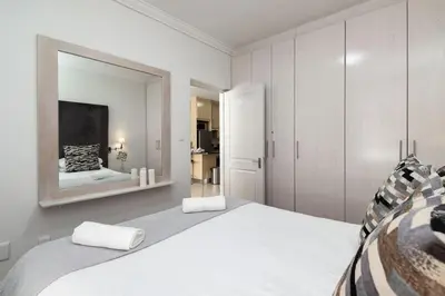 a white bedroom with a large bed and a mirror at Spacious 1 Bedroom Flat Church St Stellenbosch in Stellenbosch