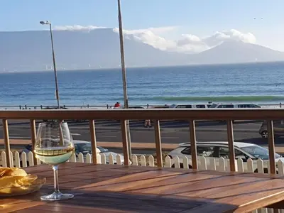 a glass of wine sitting on a table with the ocean at Bloubergstrand Beachfront Apartment Witsand 101 in Cape Town