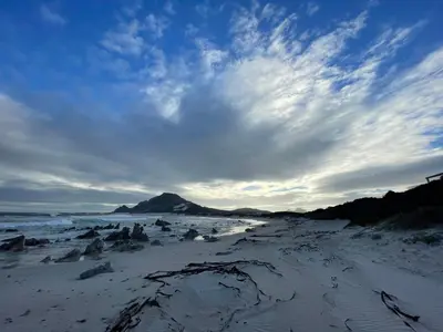a sandy beach with a cloudy sky and the ocean at Brunia Cottage in Bettyʼs Bay