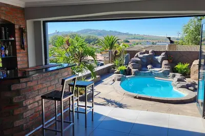a patio with a swimming pool and two stools in front of a large window at Champers with a view in Cape Town