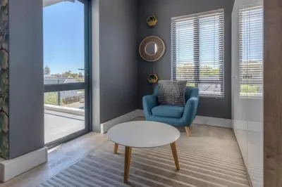 a living room with a blue chair and a table and a window at Trebuchet Studio Apartment in Somerset West