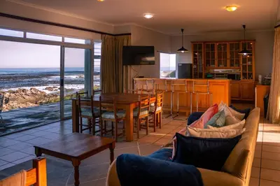 a living room with a couch and a table and a kitchen at Seascape, Vermont Retreat in Hermanus
