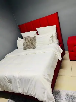 a bed with a red headboard and white sheets and pillows at Brooklyn Queens and Kings Guesthouse in Cape Town