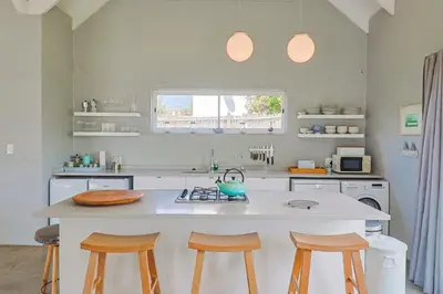 a kitchen with a counter with stools and a sink at Lily House in Bettyʼs Bay
