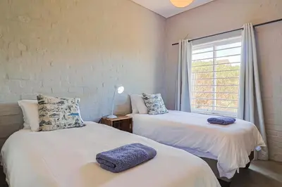 two beds in a room with a window at Lily House in Bettyʼs Bay