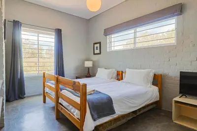 a bedroom with a bed and a tv and two windows at Lily House in Bettyʼs Bay