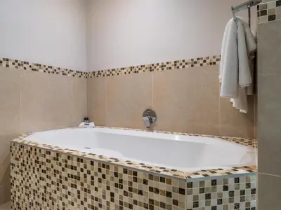 a bathroom with a tub with a tiled wall at Lagoon Shoreline Penthouse in Cape Town