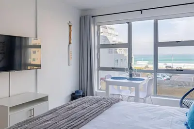 a bedroom with a bed and a view of the ocean at Beach Front Sea View Apartment, Table View in Cape Town