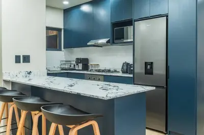 a kitchen with blue cabinets and a counter with stools at Modern Central 1 BR Apartment in Stellenbosch