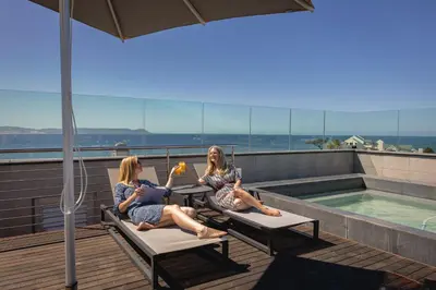 three women sitting on chairs next to a swimming pool at Sea-View Studio - Hermanus Waterfront Apartments in Hermanus