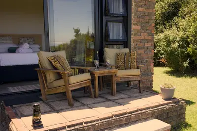 a patio with two chairs and a table and a bed at Cozy House & Studio with Sea and Mountain Views in Bettyʼs Bay