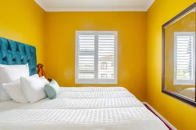 a yellow bedroom with a bed and two windows at Affordable Luxury in Cape Town