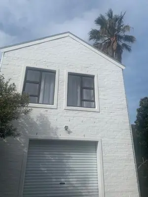 a white building with a garage door and a palm tree at Two Palms Cottage in Hermanus