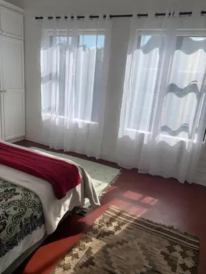 a bedroom with white curtains and a bed with a rug at Two Palms Cottage in Hermanus