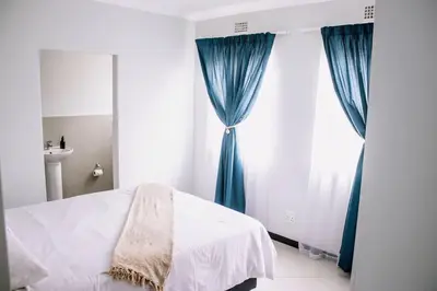 a bedroom with a bed and a window with blue curtains at 7 on Laibach - Buhrein Estate, Kraaifontein in Cape Town