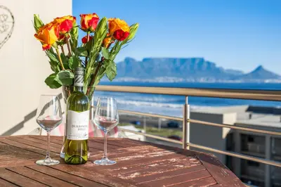 a table with two glasses and a bottle of wine and flowers at The Waves 302 in Cape Town