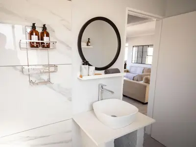 a white bathroom with a sink and a mirror at Seaside Serenity in Hermanus