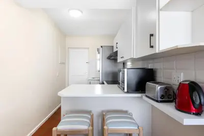 a kitchen with white cabinets and a counter with stools at Sea Spray A410 in Cape Town