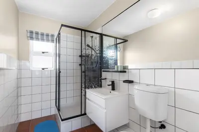 a white tiled bathroom with a toilet and a shower at Sea Spray A410 in Cape Town
