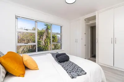a white bedroom with yellow pillows and a large window at Surfside Haven, 3 Bed Townhouse in Cape Town