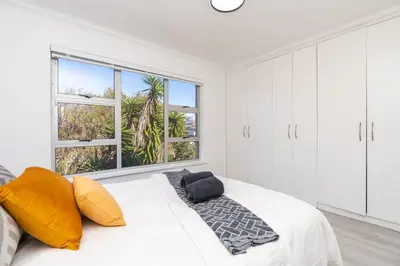 a bedroom with a bed with yellow pillows and a window at Surfside Haven, 3 Bed Townhouse in Cape Town