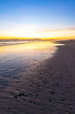 a sandy beach with the sun setting in the ocean at Soete Rus Strand in Cape Town