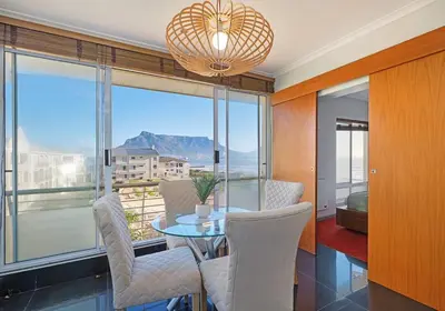 a dining room with a table and chairs and a large window at Modern Cape Town Beach Apartment in Cape Town