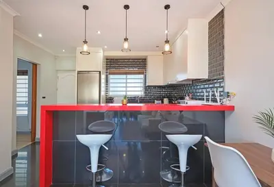 a kitchen with a red counter and stools at Modern Cape Town Beach Apartment in Cape Town