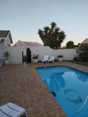 a swimming pool with two white chairs next to a wall at Mountain View Apartment in Cape Town