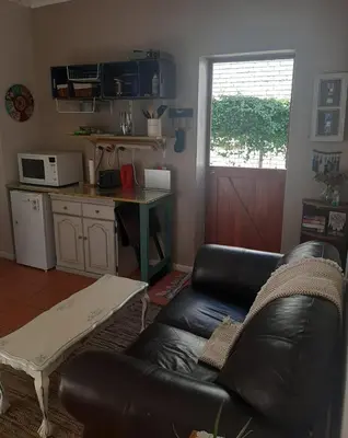 a living room with a black leather couch and a table at Voëlklip garden flat in Hermanus