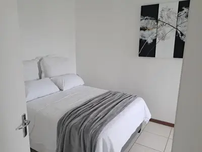 a white bedroom with a bed with white sheets at 8 Marina Sands beach apartment in Cape Town